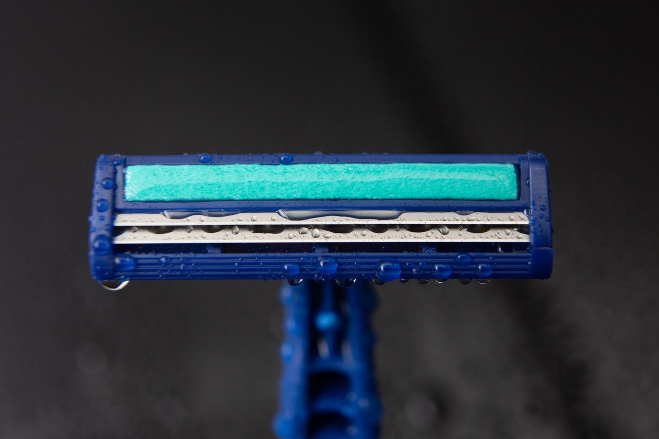 blue disposable razor blade, on black background with water drops