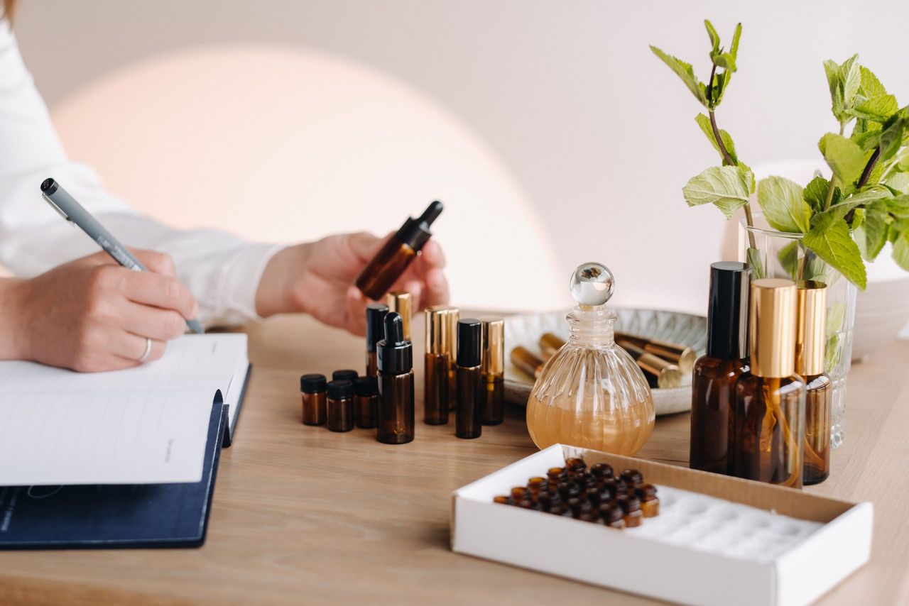 Close-up of female hands holding a bottle of essential oil and writing an entry in a notebook, aromatherapy.