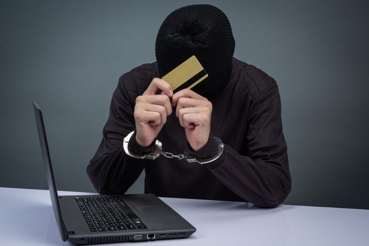 Thief wearing a black hat, obscuring the face, was arrested on a gray background.