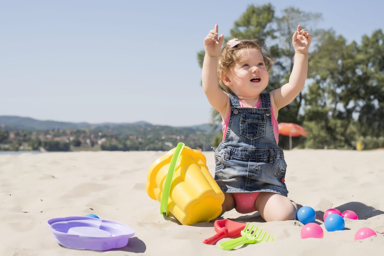 An adorable little girl playing on the beach with colorful balls and plastic toys