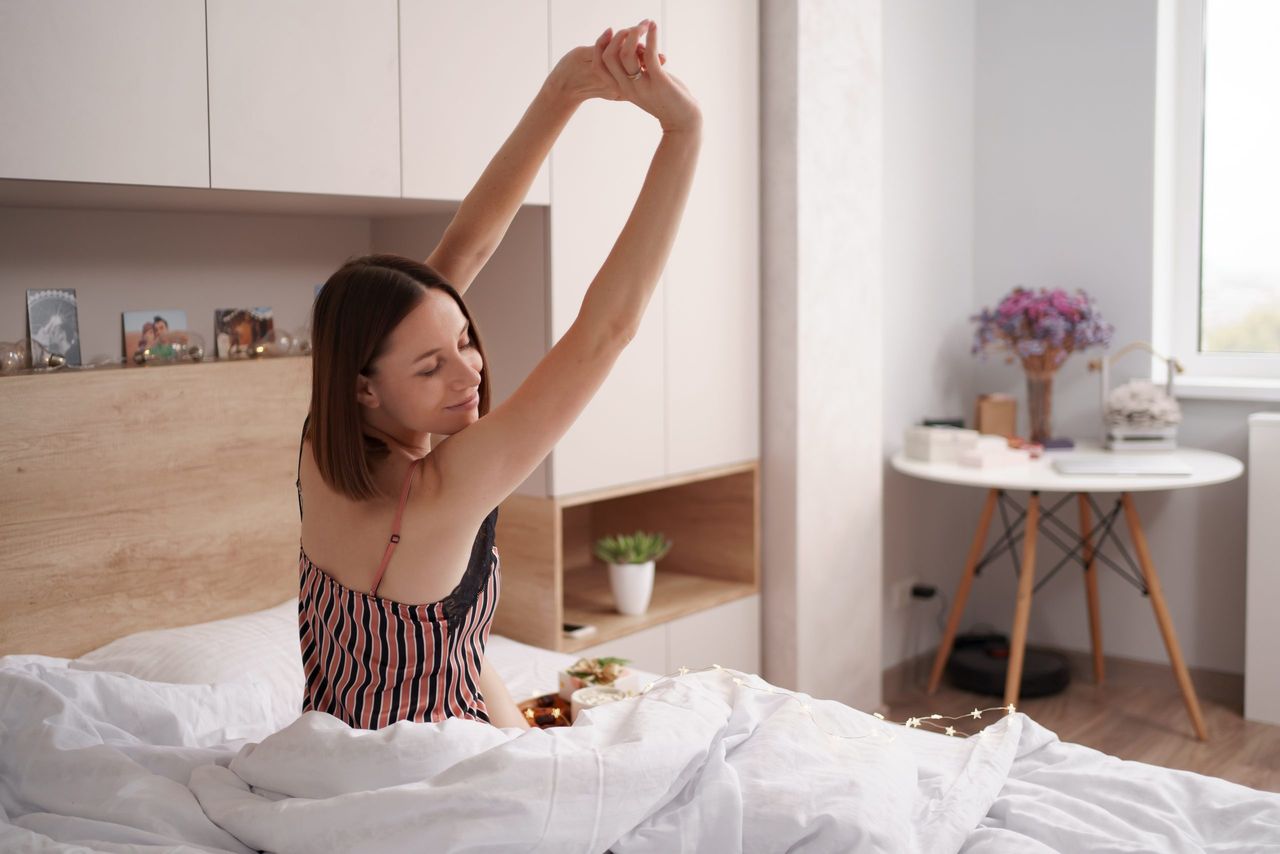 Women enjoying coffee with marshmallows on the bed with present near her while stretching after awaking. Morning surprise