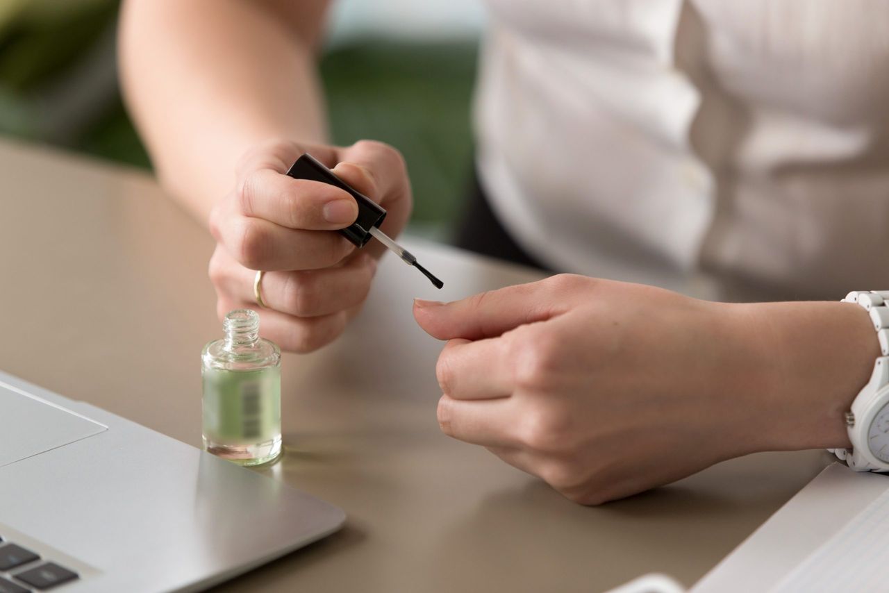 Close up view of female hands on office desk making manicure, applying lacquer, painting nails near laptop, bored lazy woman has nothing to do at work, employee misconduct in workplace, wasting time