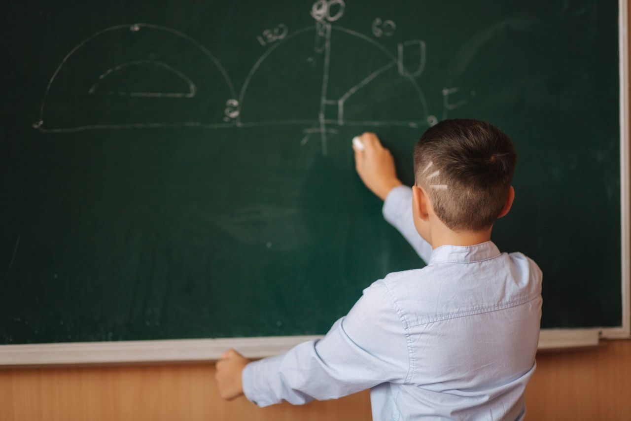 Little boy white down something on blackboard. Clever male.