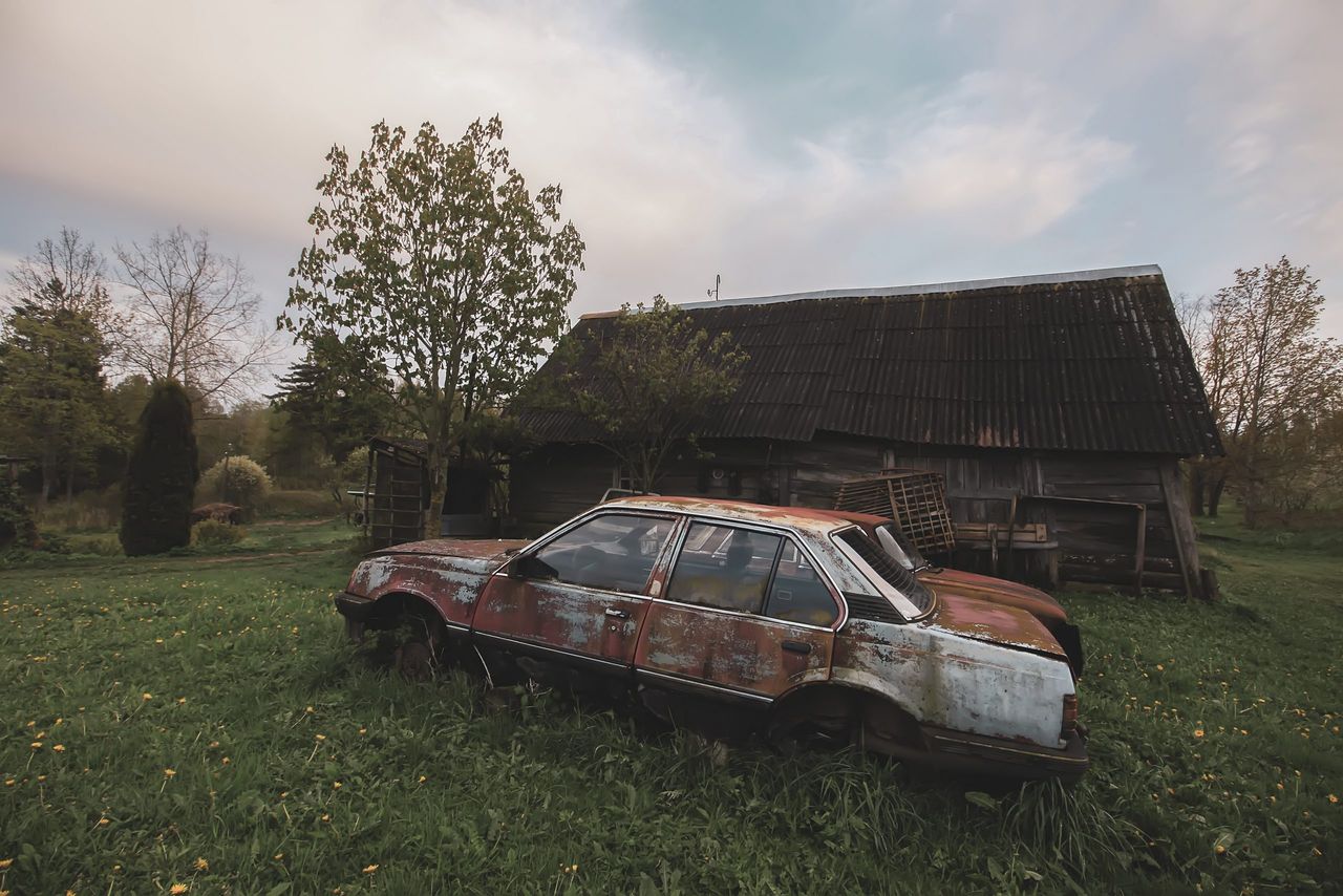 Abandoned rusty soviet car on rural backyard with wooden buildings