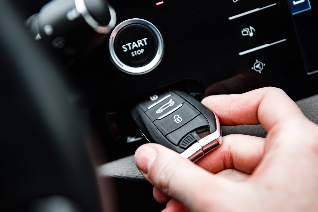 Hand insert car keyless remote in a keyhole in a car with start engine button.