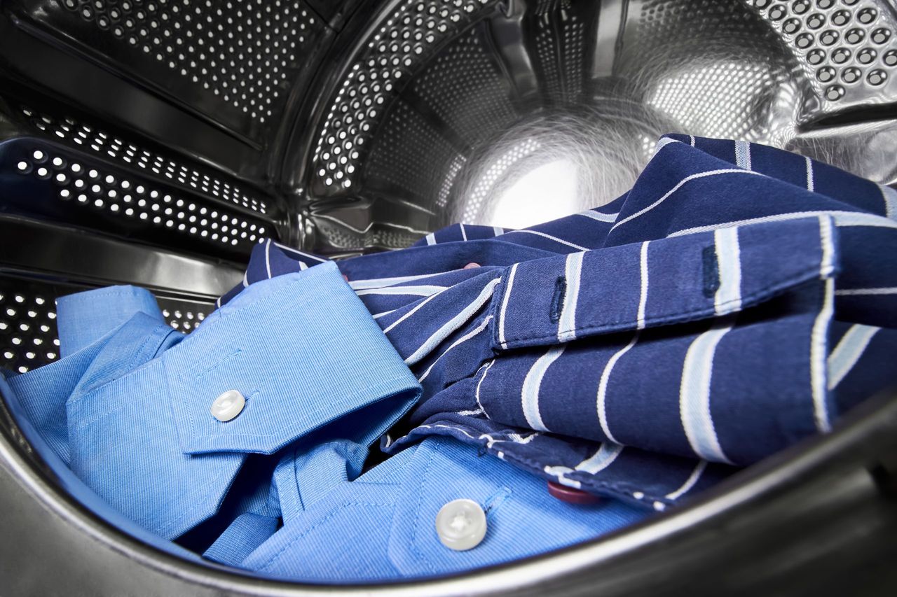 Close-up of an open door in washing machine with dirty shirts inside