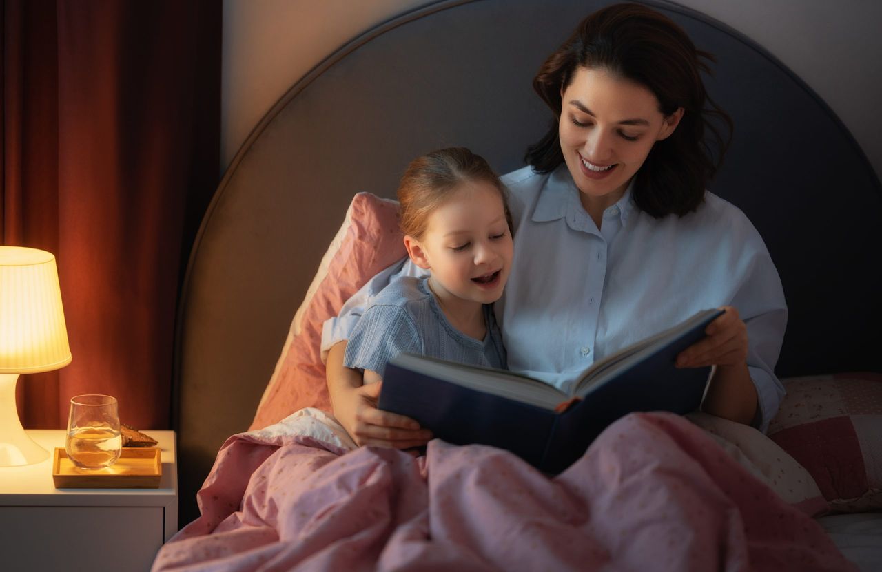 Happy loving family. Pretty young mother reading a book to her daughter on the bed at home.