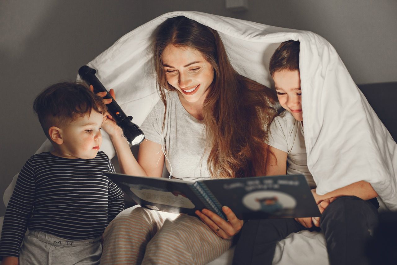 Family under the blanket in bed. People at home.