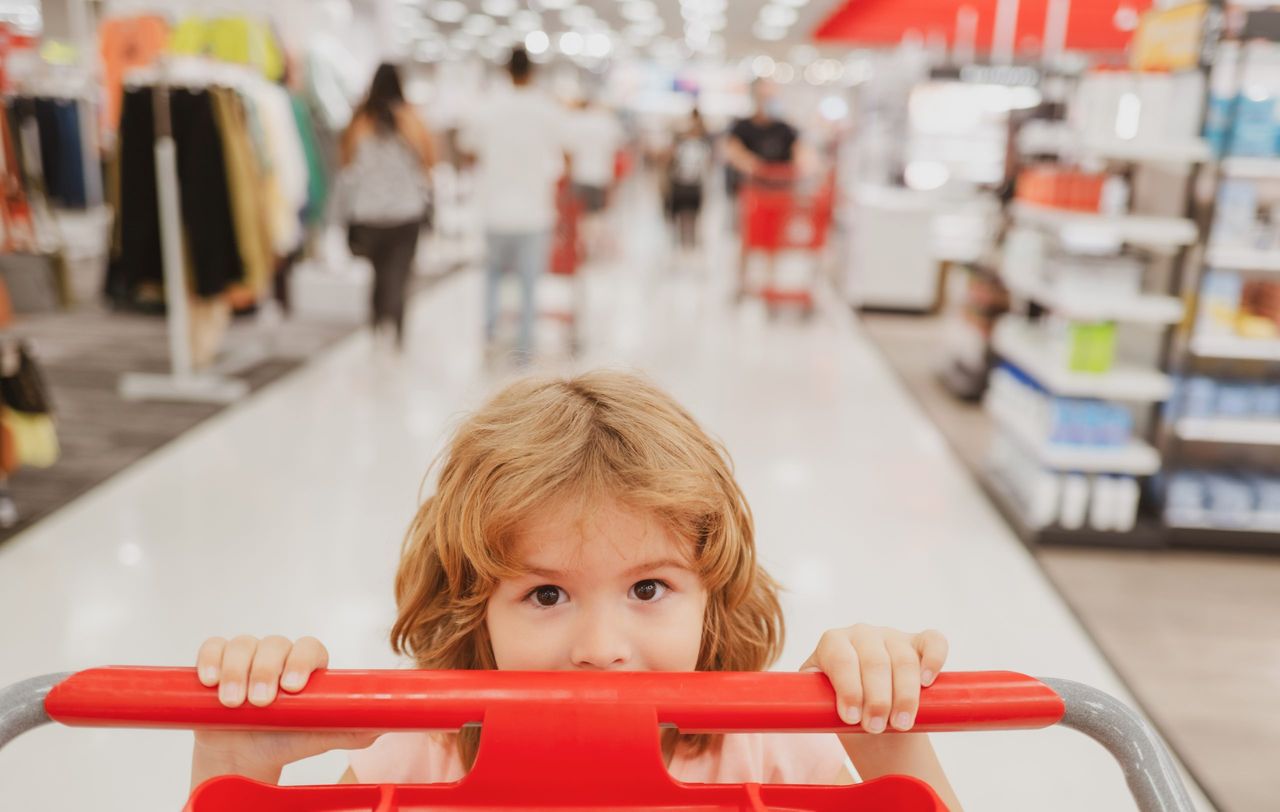 Closeup portrait of kid at grocery or supermarket with goods in shopping trolley