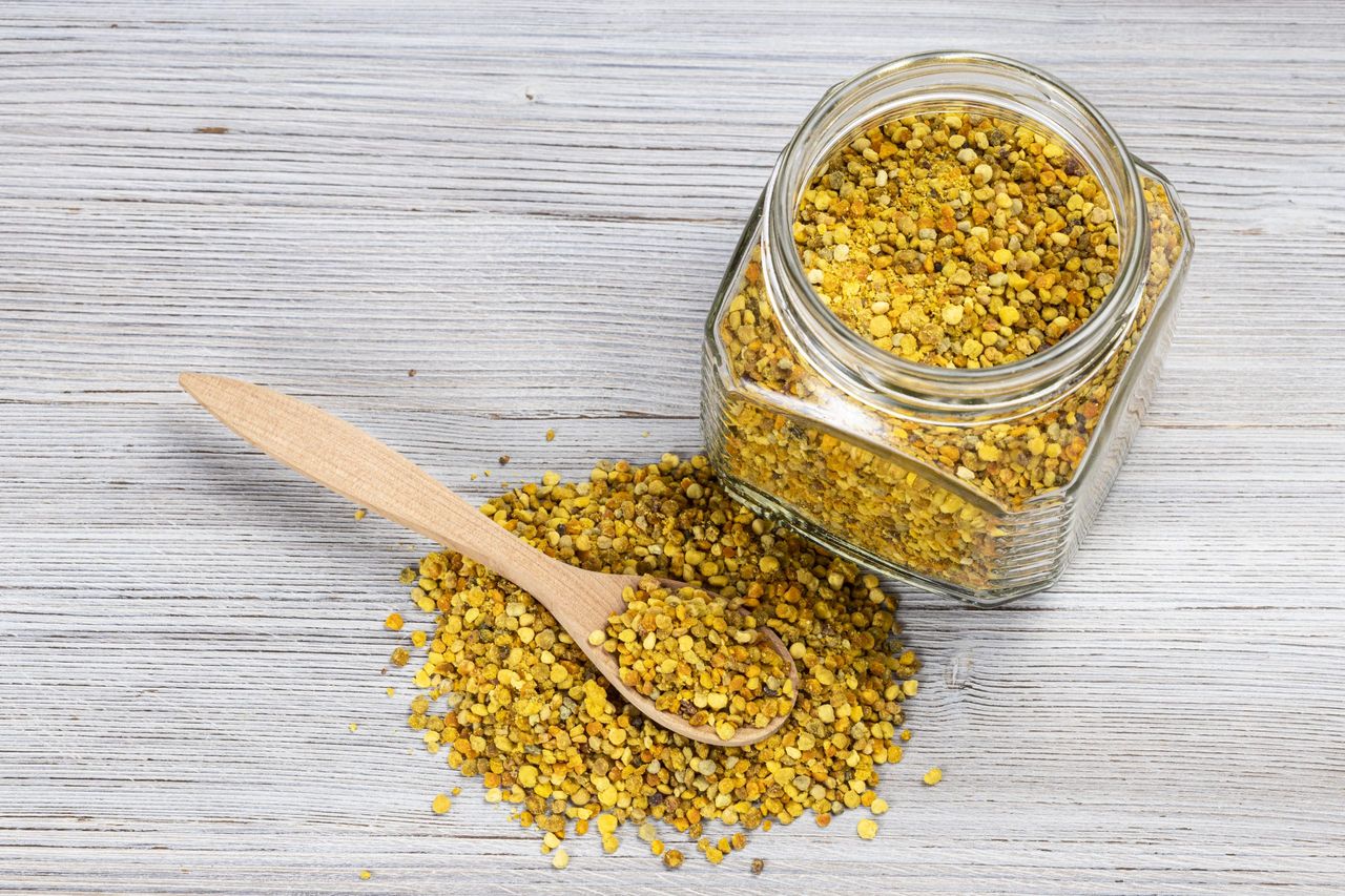 above view of glass jar and spoon in pile of natural bee pollen on gray wooden board