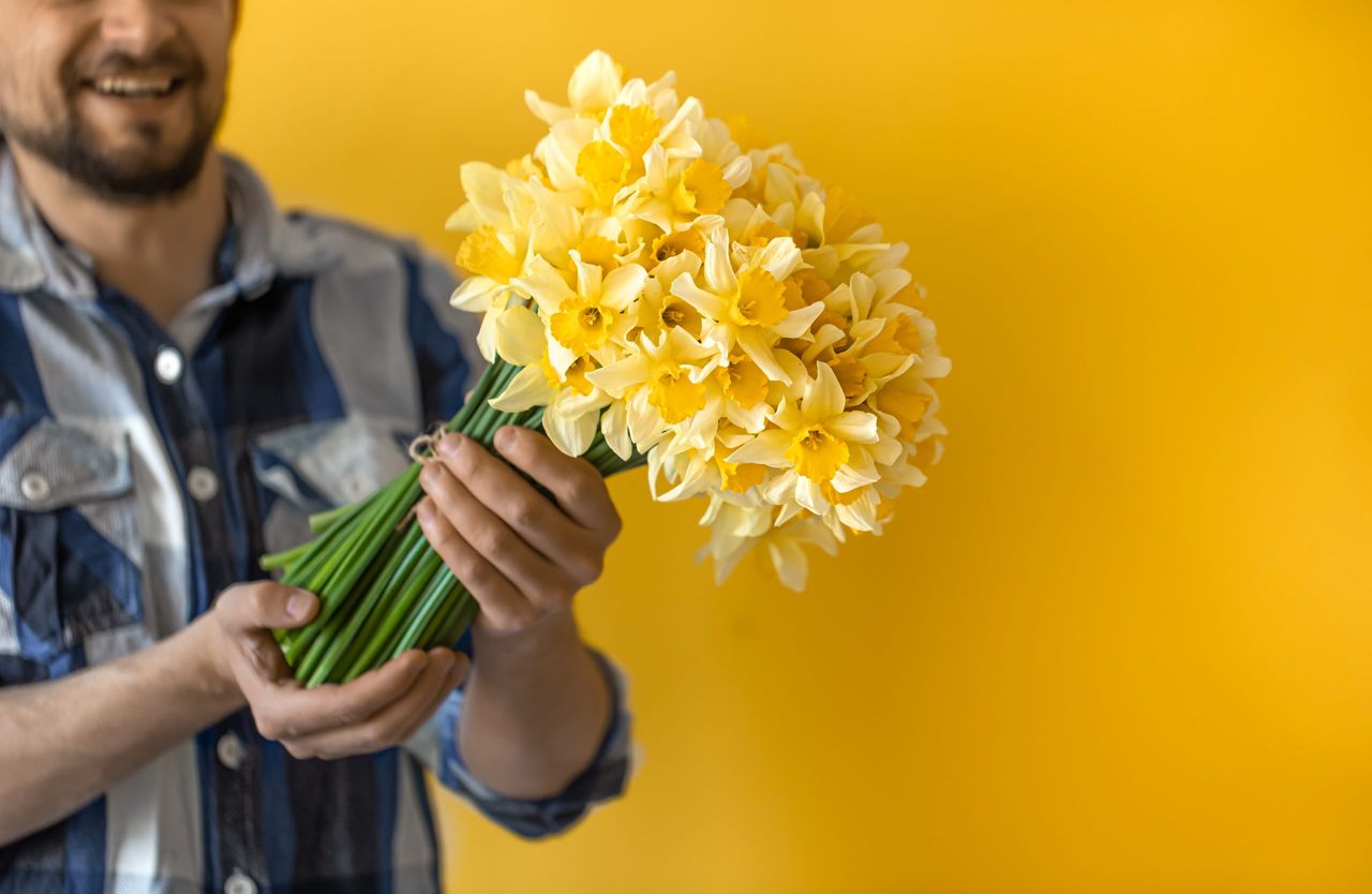 A young smiling man with a bouquet of spring flowers on a colored background. The concept of greetings and women's day.