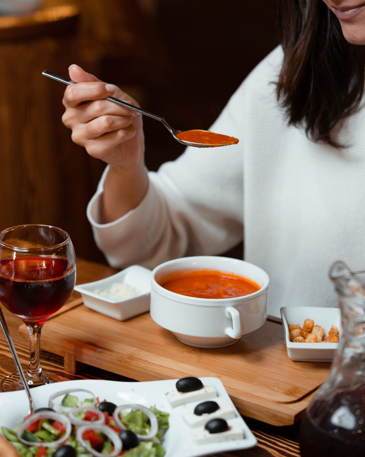 woman eating tomato soup with bread stuffing, a glass of wine