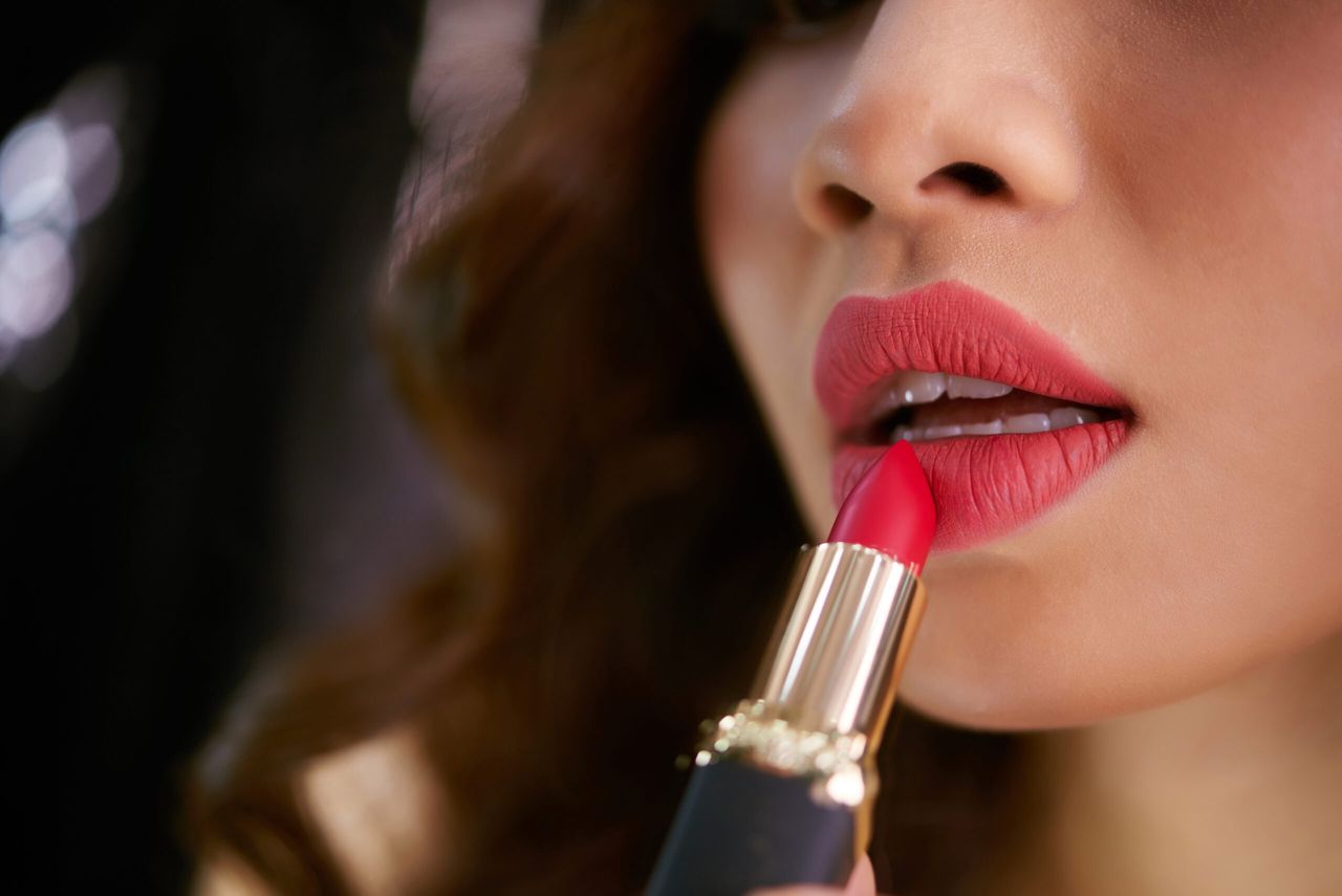 Close-up image of woman applying red lipstick to her plump lips