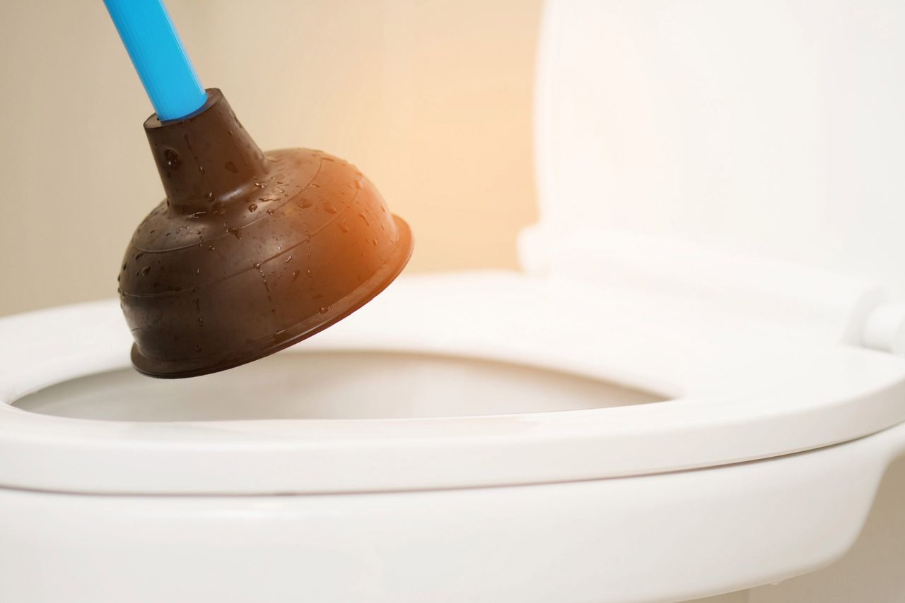 Serviceman repairing toilet with hand plunger. Clogged toilet.