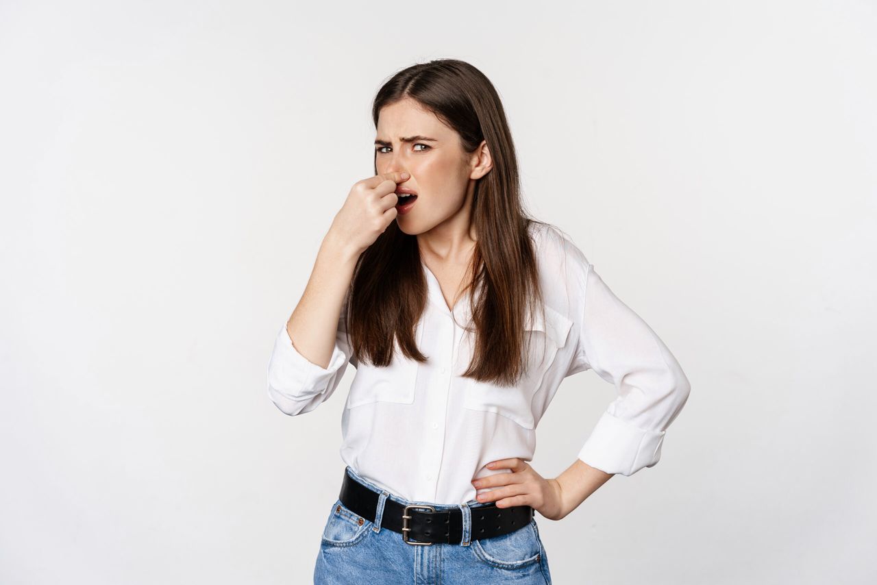 Disgusted adult woman, 25 years old, shut nose from dislike and disgust, bad smell, standing over white background. Copy space