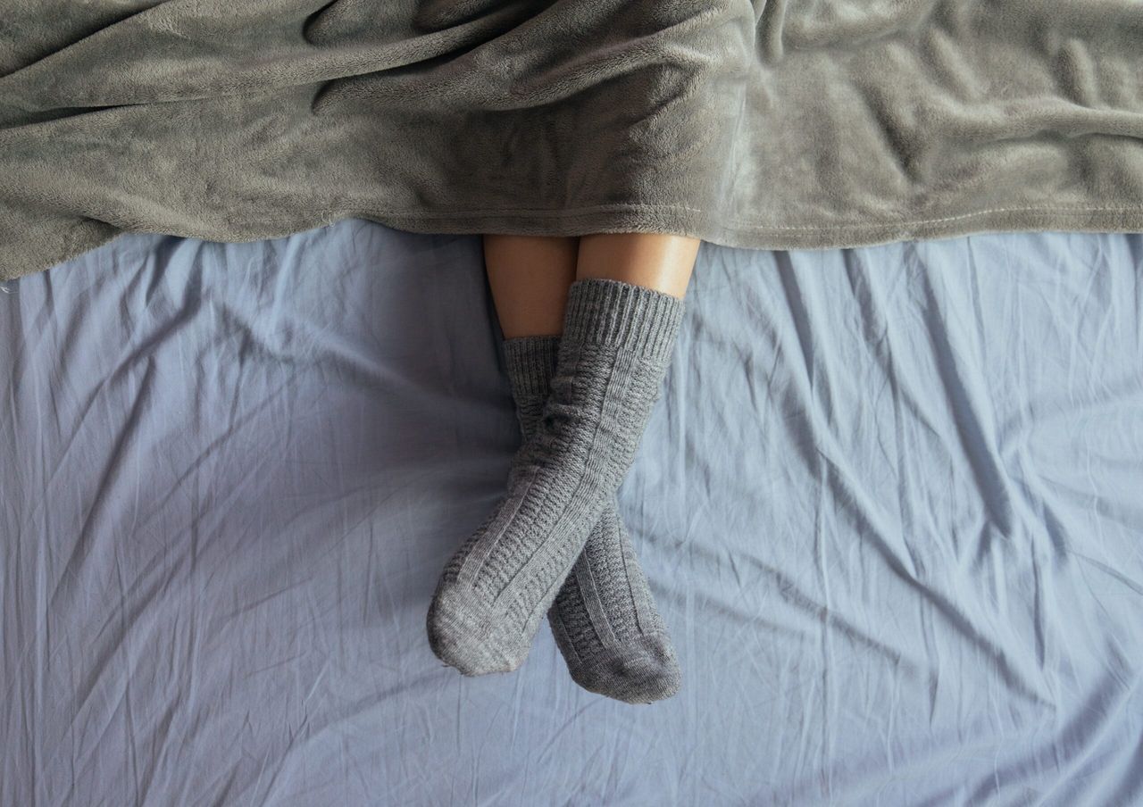 A high angle shot of the legs of a female in grey knitted socks under the blanket