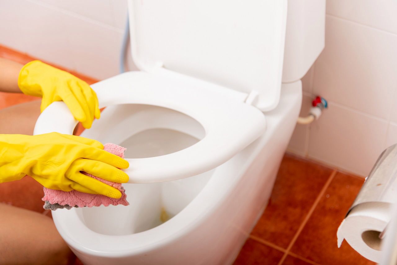 Hands of Asian woman cleaning toilet seat by pink cloth wipe restroom at house, female wearing yellow rubber gloves she sitting and cleanup or washing bathroom, Housekeeper healthcare concept