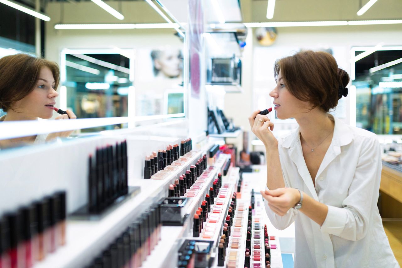 Caucasian female tries on colourful lipstick at beauty corner