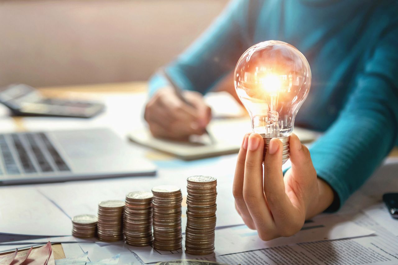 business woman hand holding lightbulb with coins stack on desk. concept saving energy and money