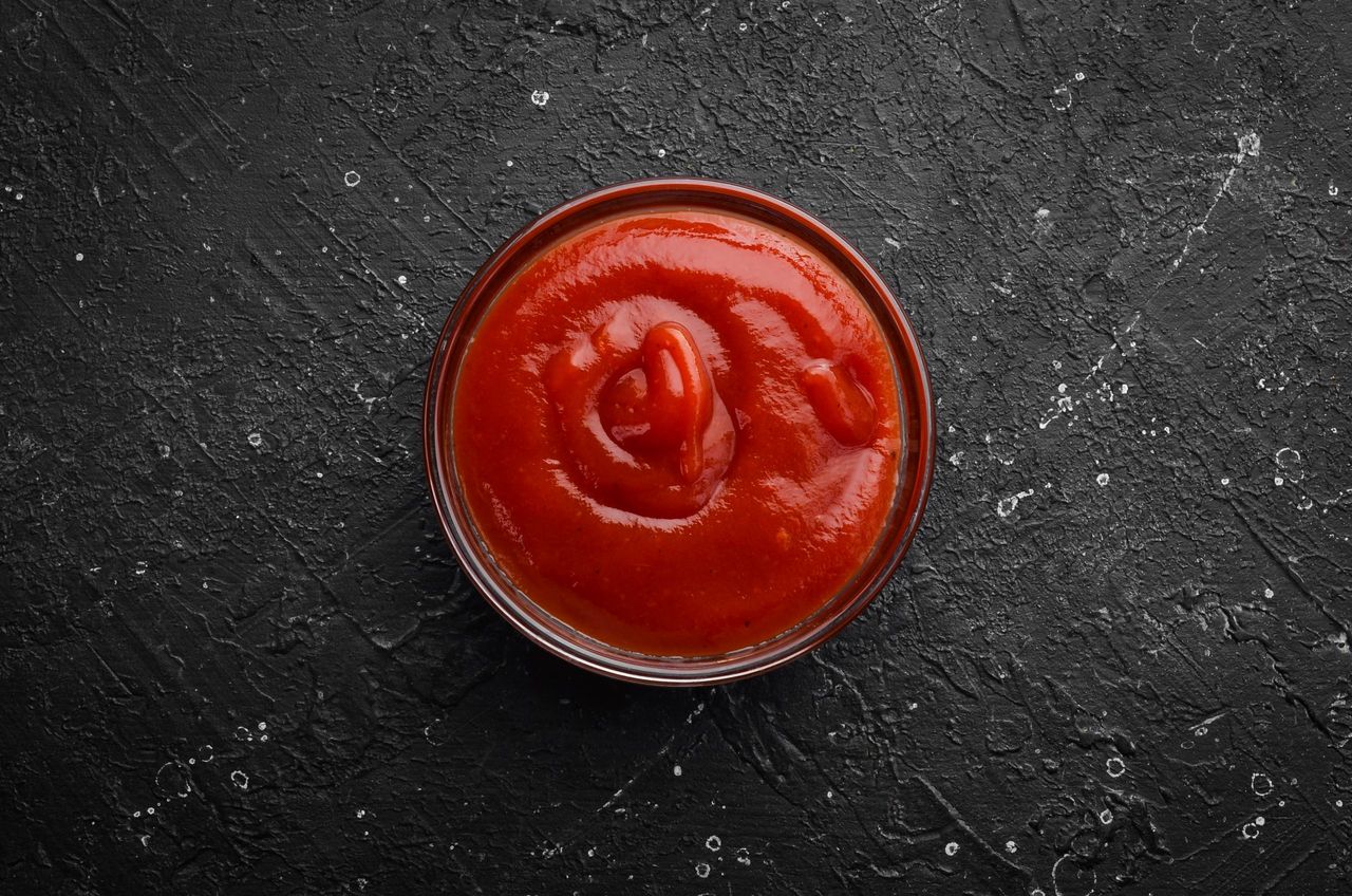 Ketchup sauce. Tomato paste in a bowl on a black stone background. Top view. Free copy space.
