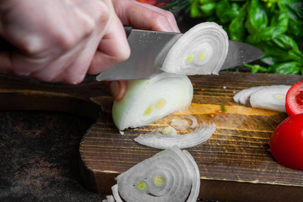 Housewife cutting onion for salad on wooden board close-up