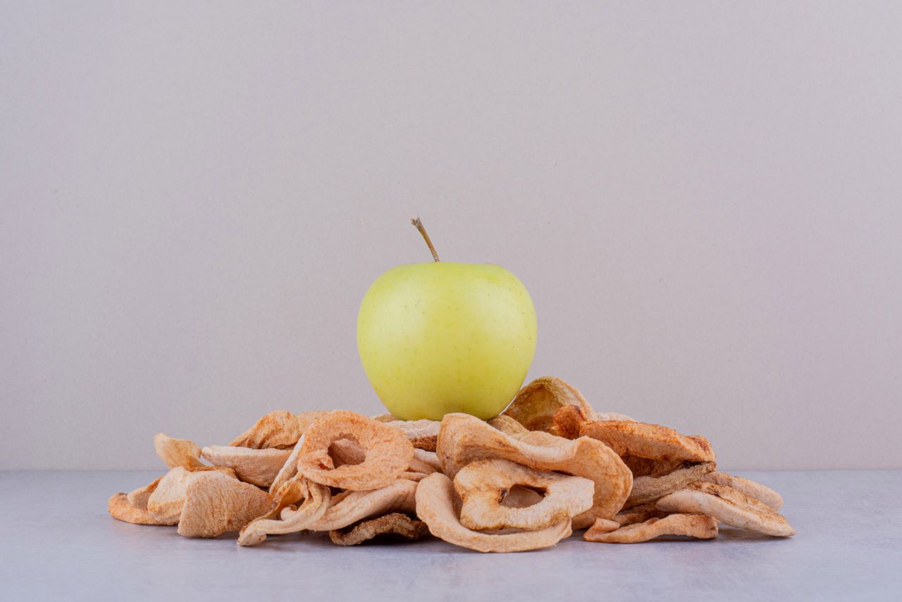 Green apple sitting on a pile of dried apple slices on white background. High quality photo