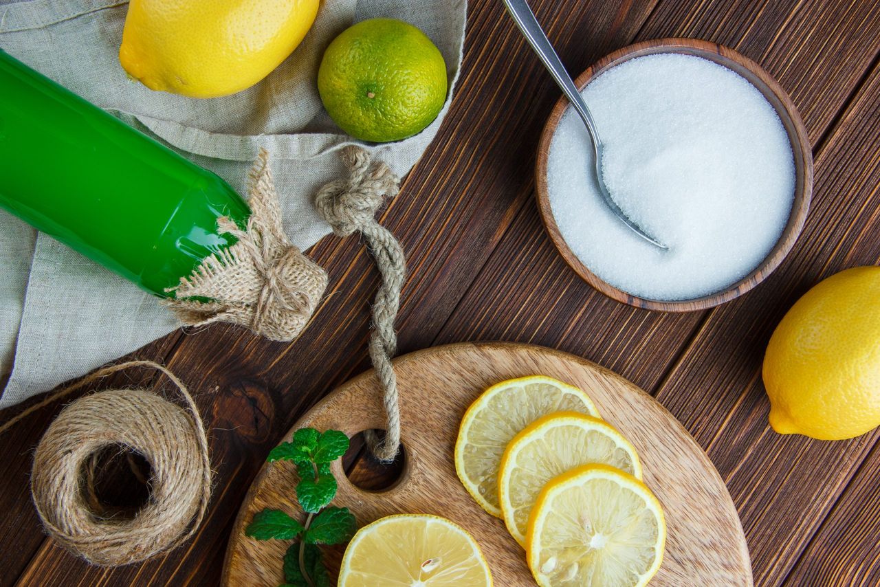 Lemons with lime, herbs, drink, cutting board, salt, thread flat lay on wooden and kitchen towel background