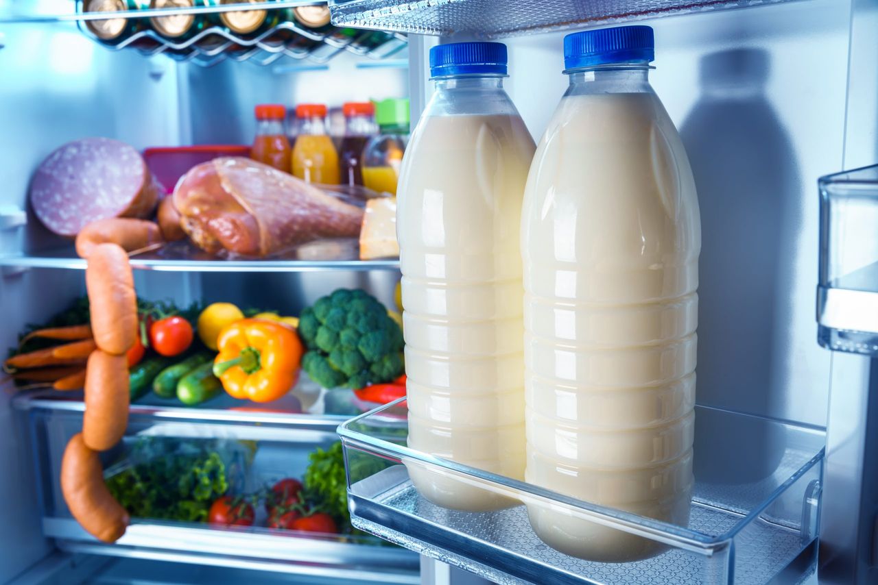 Open refrigerator filled with food. Focus on Bottles of milk in the fridge
