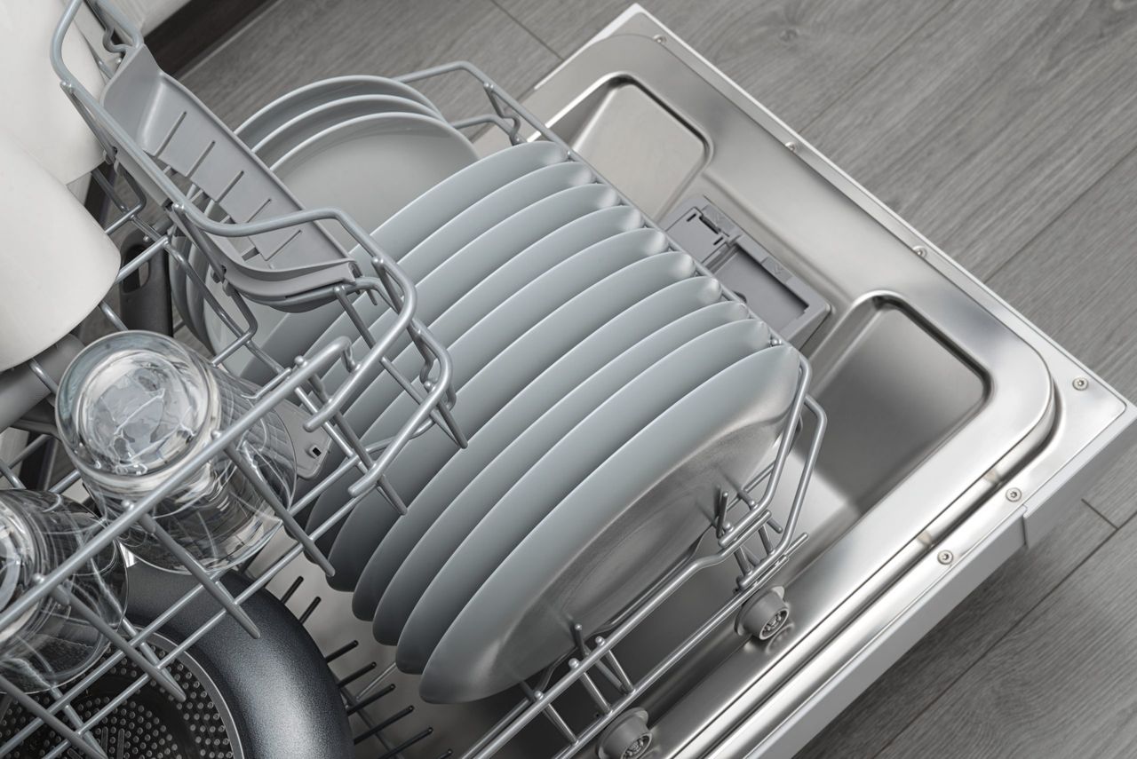 Opened domestic dishwasher with cleaned dishware in kitchen interior