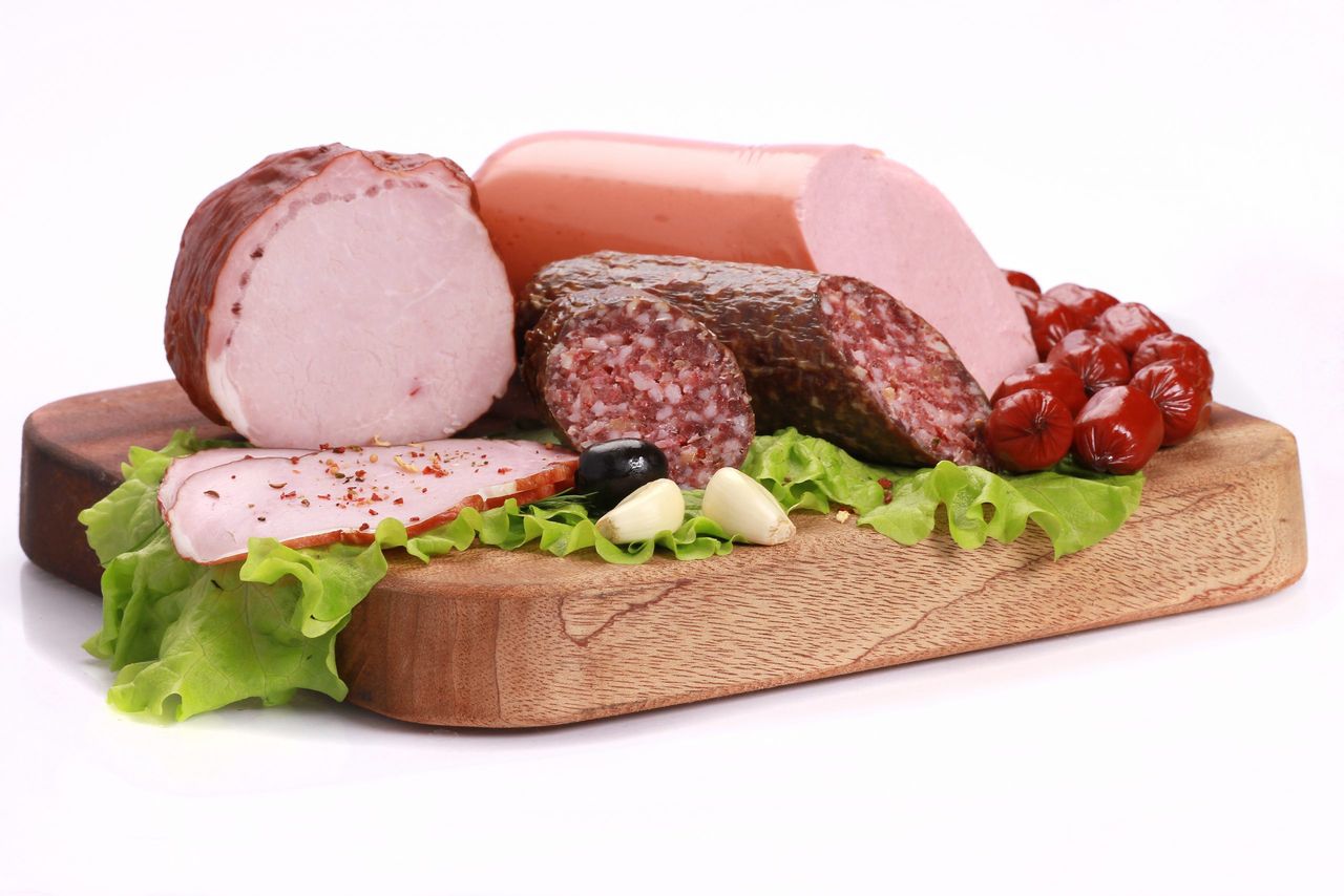 A closeup shot of slices of sausages with green lettuce on a wooden board