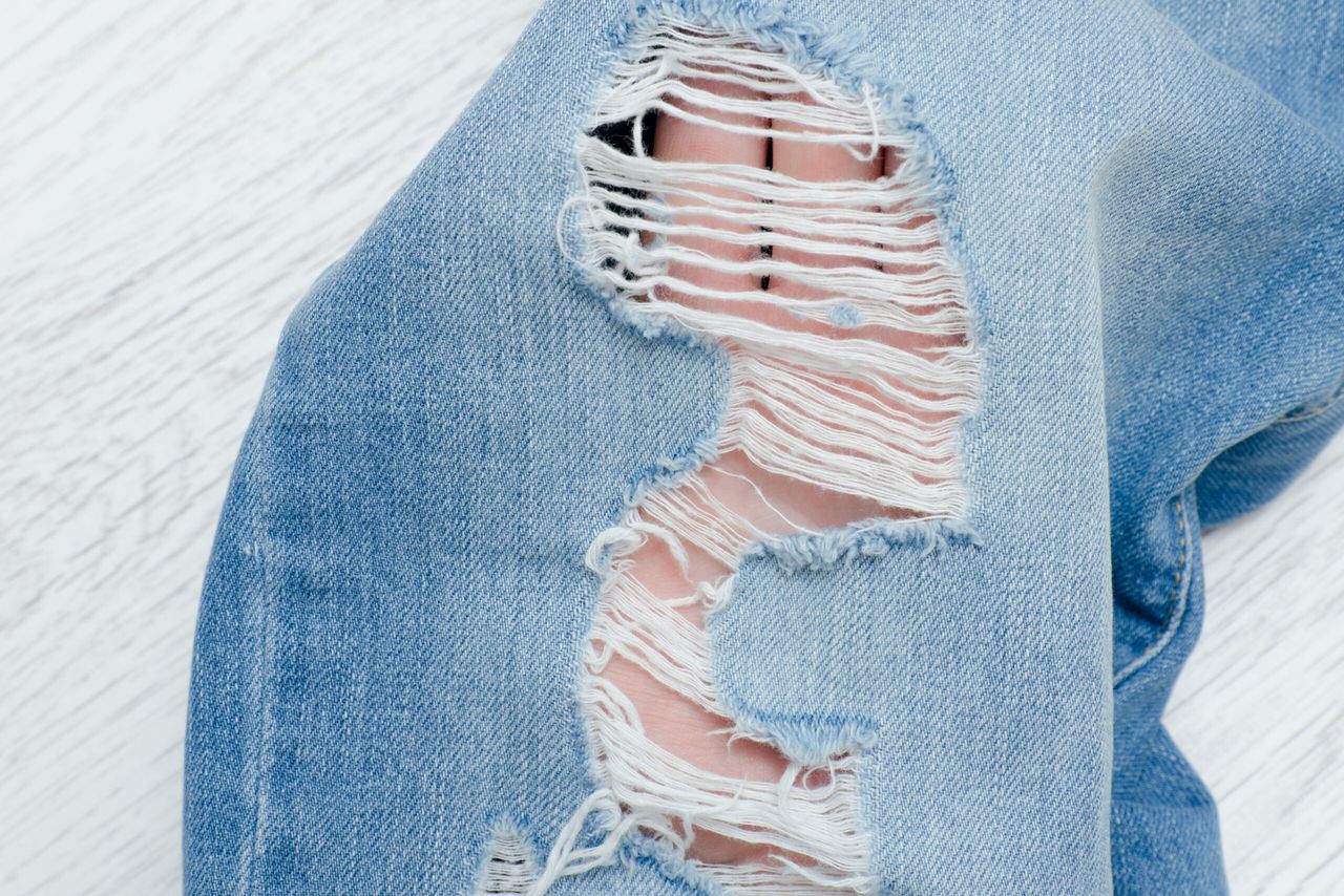 Part of blue ripped jeans. Details close-up