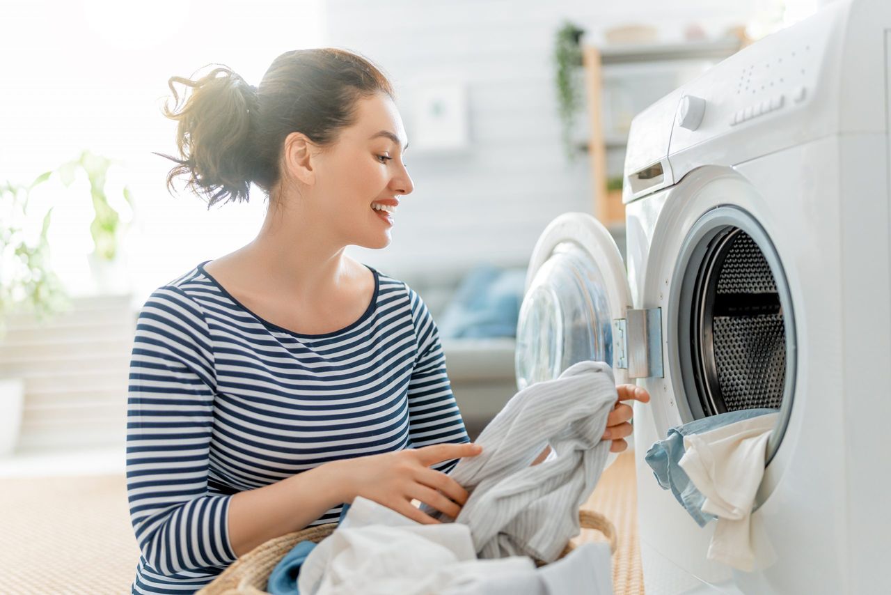 Beautiful young woman is smiling while doing laundry at home.