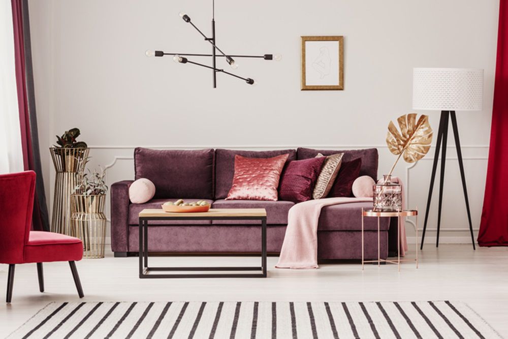 Gold leaf on copper table in sophisticated living room interior with striped carpet and violet sofa 