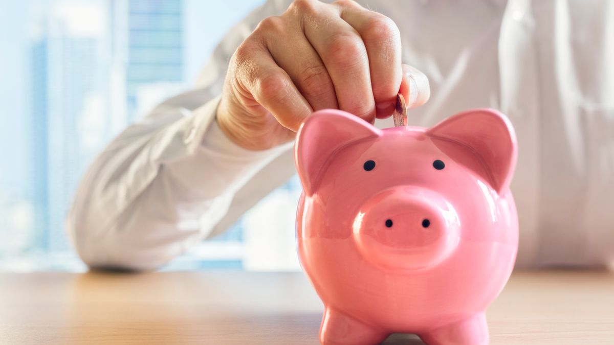 Man putting a coin into a pink piggy bank concept for savings and finance