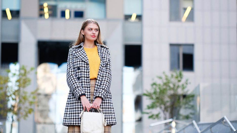 Blond hair young woman in check skirt against modern building. Street fashion style concept.
