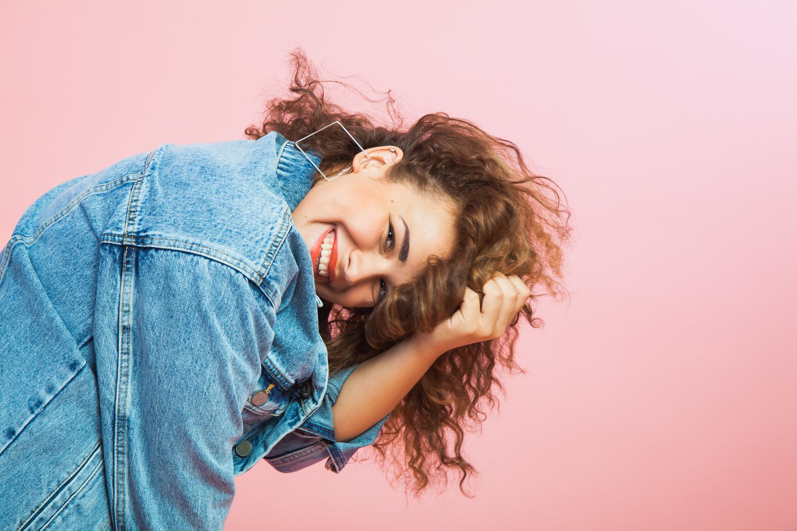 Beautiful young woman with curly hair in denim clothes. Trendy look, positive emitions, smile, copy space
