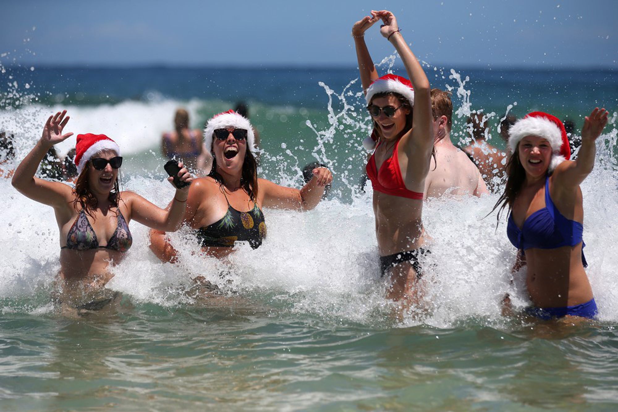 Marlies Noordeloos of the Netherlands, left, Lisa Van De Velde of Belgium, second left, Charlotte Trotter of Britain, second right, and Viktoria Sardarian of Lithuania wear Santa hats while in the surf at Bondi Beach celebrating Christmas Day in Sydney, Australia, Friday, Dec. 25, 2015. (AP Photo/Rick Rycroft) 