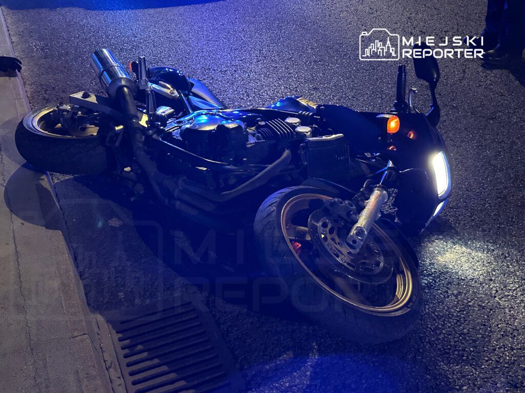 Motocykl leżący na boku na drodze, otoczony niebieskim światłem, w nocy.