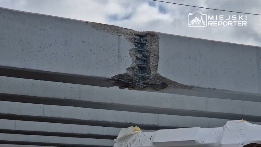 Uszkodzona belka betonowa z widocznymi pęknięciami i odsłoniętą stalową zbrojeniem w konstrukcji budowlanej.