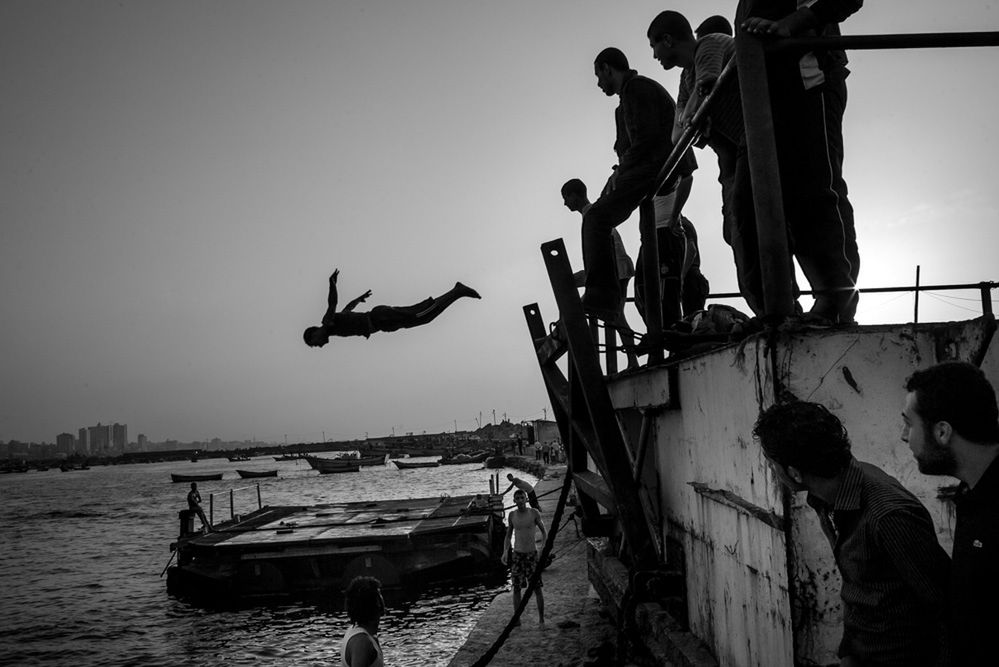 Młodzież w niedzielne popołudnie korzysta z otwartej bramy w porcie w mieście Gaza. Niestety skoki odbywają się wprost do zanieczyszczonej wody.