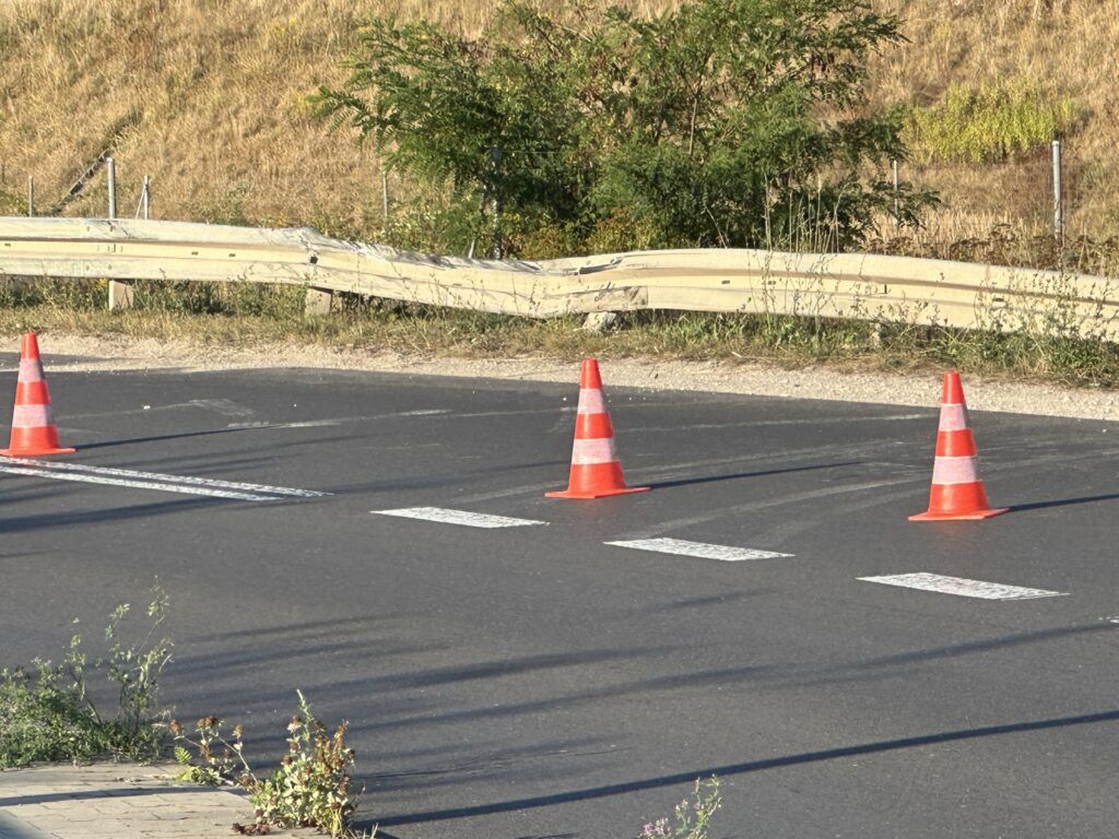 Czerwone pachołki drogowe ustawione na asfalcie, blokujące przejazd w kierunku wyznaczonego przejścia dla pieszych.
