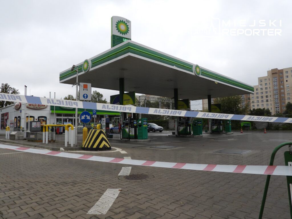Stacja benzynowa z oznaczeniem BP, ogrodzona taśmą policyjną, w tle bloki mieszkalne.
