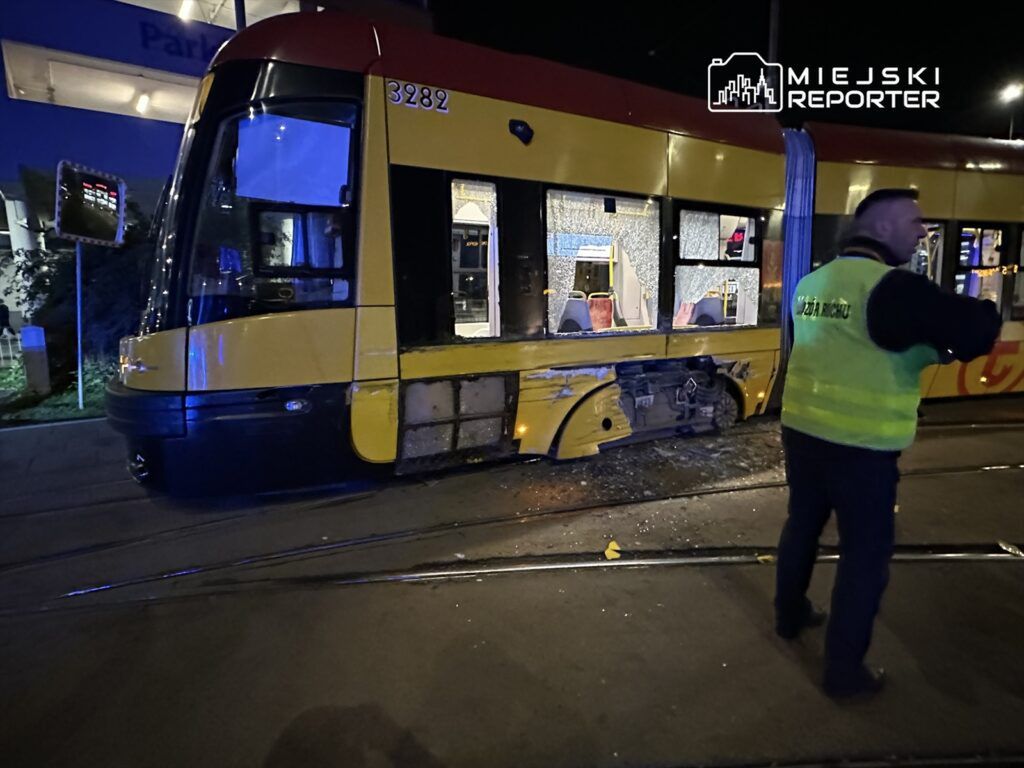 Tramwaj z uszkodzoną boczną częścią stoi na torach, a obok niego mężczyzna w kamizelce odblaskowej kieruje ruchem.