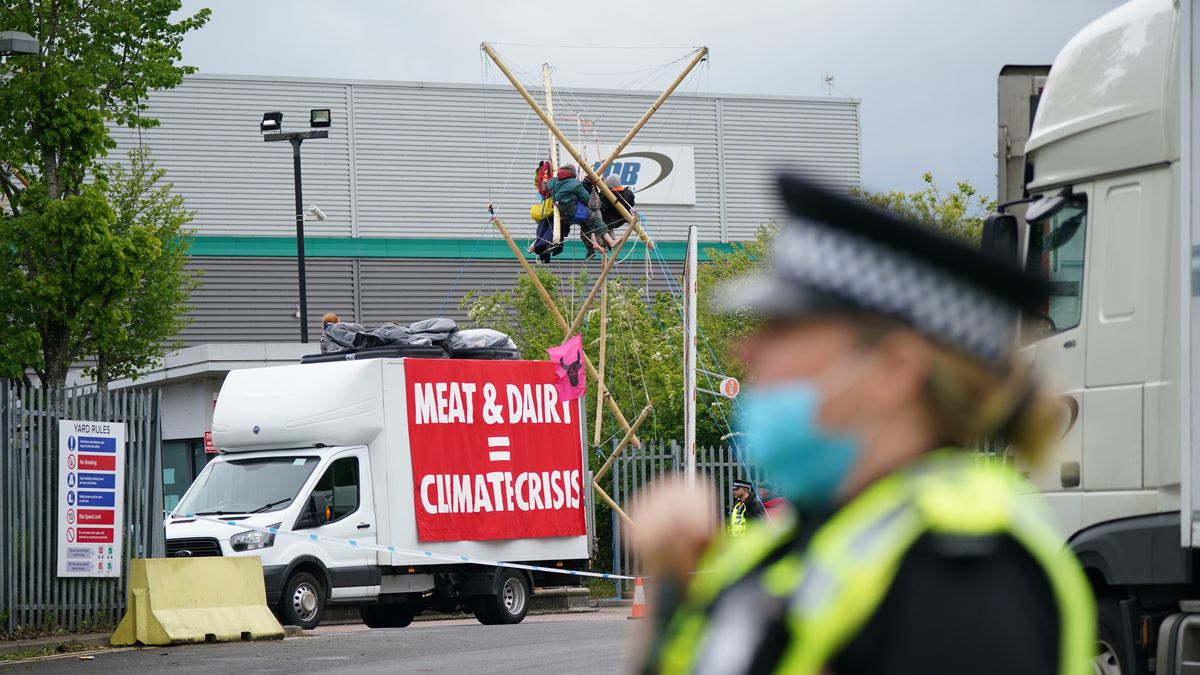 Police officer in front of Animal Rebellion protesters suspended from a bamboo structure and on top of a van outside a McDonalds distribution site in Hemel Hempstead, Hertfordshire, which is being blockaded to stop lorries from leaving the depot. Picture date: Saturday May 22, 2021. (Photo by Yui Mok/PA Images via Getty Images)