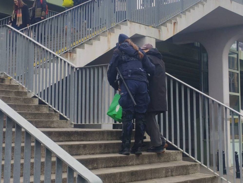 Funkcjonariusz policji pomaga osobie w pokonywaniu schodów w miejskim otoczeniu.