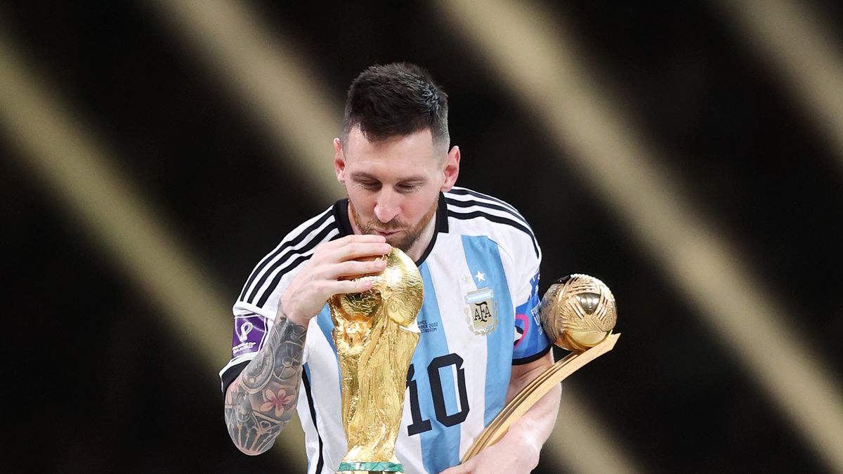 LUSAIL CITY, QATAR - DECEMBER 18: Lionel Messi of Argentina kisses the FIFA World Cup Winners' Trophy while holding the adidas Golden Boot award after the FIFA World Cup Qatar 2022 Final match between Argentina and France at Lusail Stadium on December 18, 2022 in Lusail City, Qatar. (Photo by Julian Finney/Getty Images)