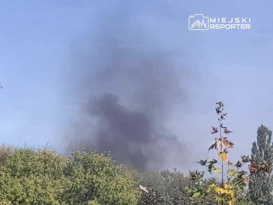 Czarny dym unoszący się z zadrzewionego terenu pod błękitnym niebem.