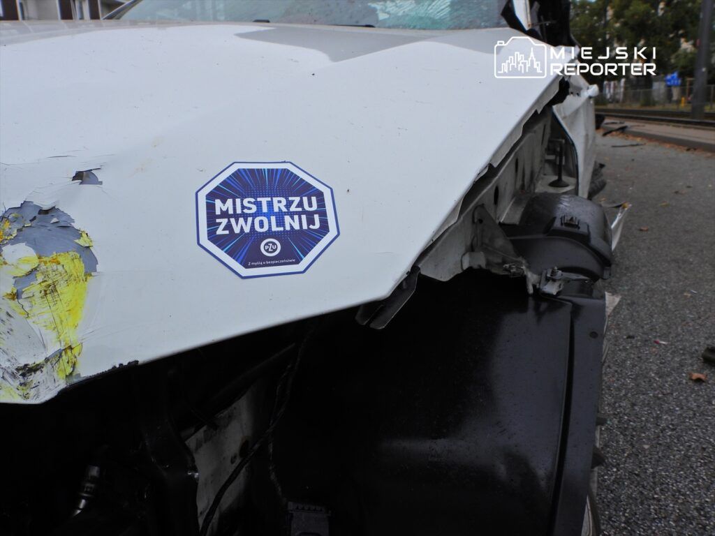 Zniszczony pojazd z wyraźnymi śladami uszkodzeń oraz naklejką „MISTRZU ZWOLNIJ” na karoserii.