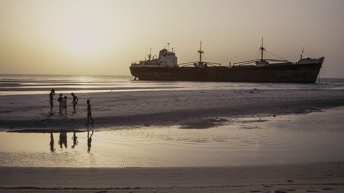 STRAIT OF HORMUZ - OCTOBER 1987: Children playing on a beach with a tanker in the background that was run aground in the Arabian Gulf during the tanker war of 1987 when Iran attacked vessels sailing to ports in the Gulf. (Photo by Derek Hudson/Getty Images)