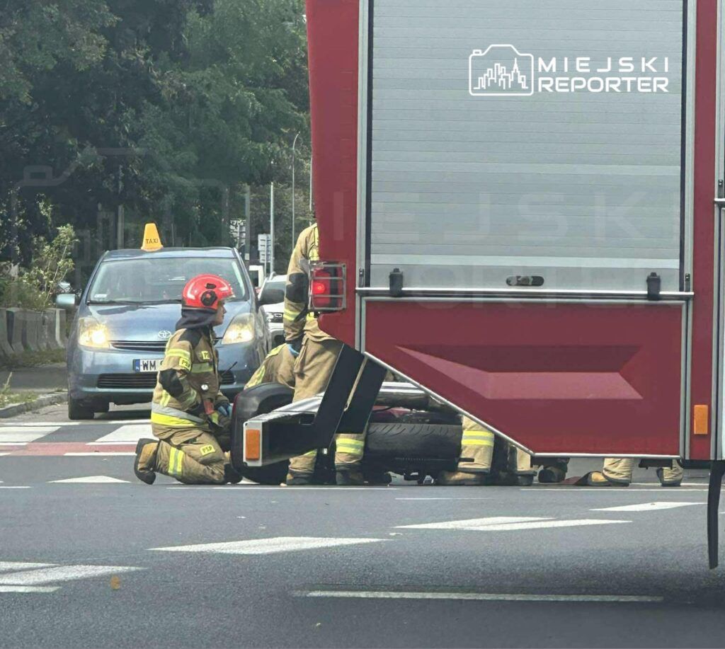 Strażacy w mundurach zajmują się usuwaniem uszkodzonego pojazdu na ruchliwej ulicy.